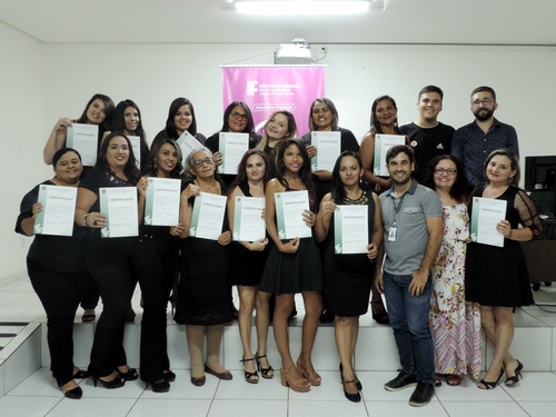 Com certificado em mãos, mulheres posam para foto ao lado do coordenador de extensão, da coordenadora do projeto e de professores do curso.